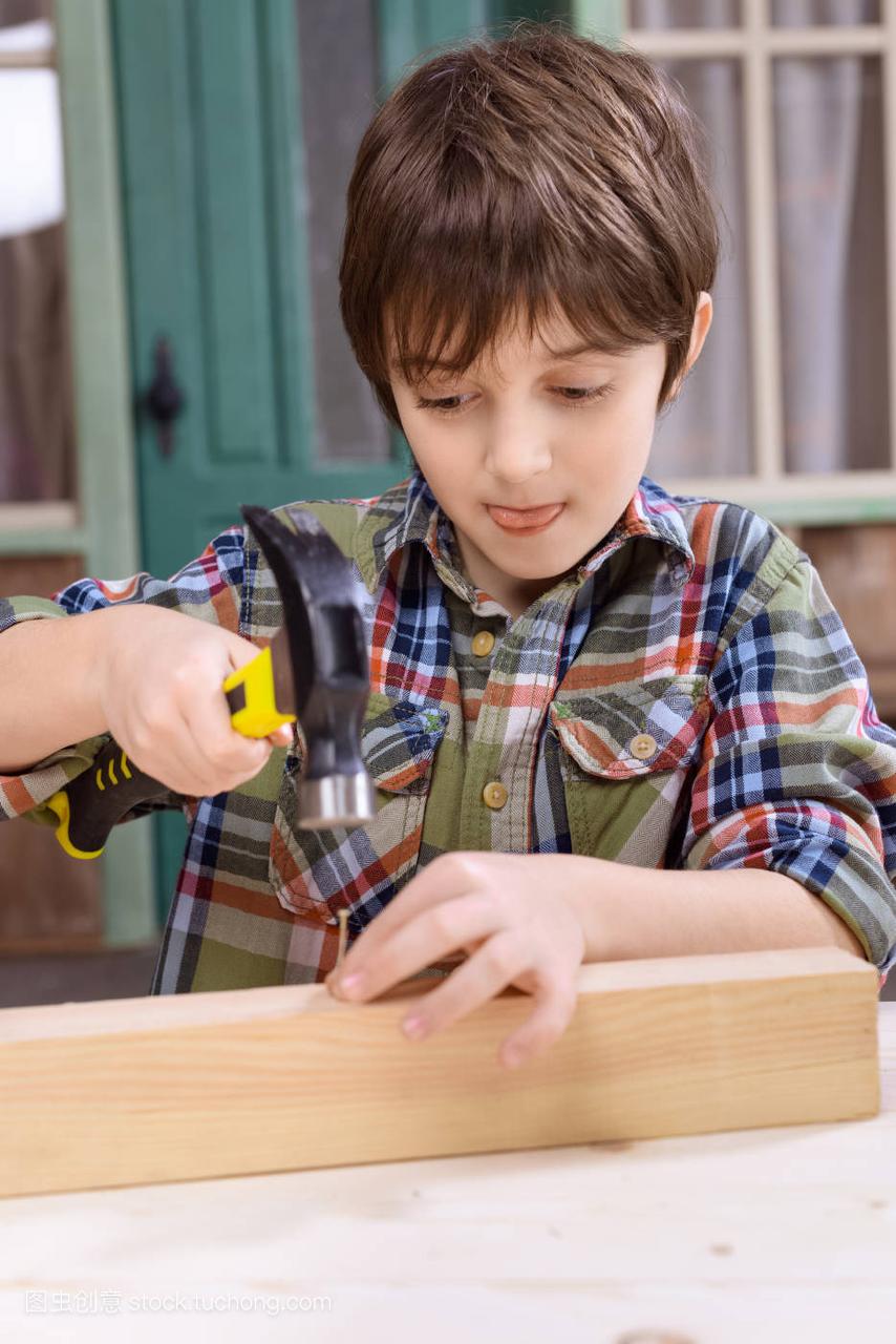 小男孩穿着格子衬衫在木板上钉钉子
