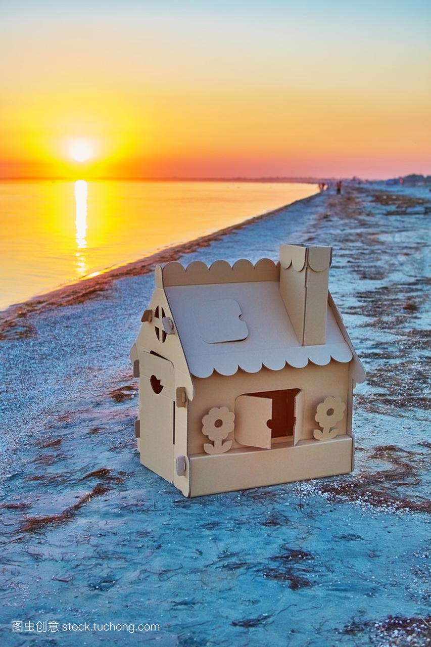 在日落时做的瓦楞纸板在海洋海岸的玩具房子