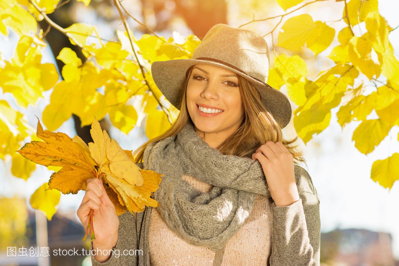 现代美丽的年轻女子在公园在秋天举行的叶子