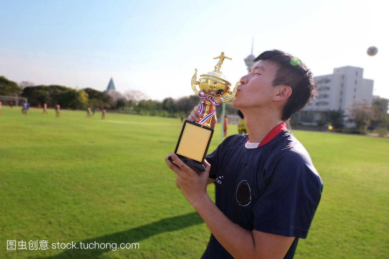 亚洲足球球员男人亲吻奖杯,庆祝他优胜者冠军