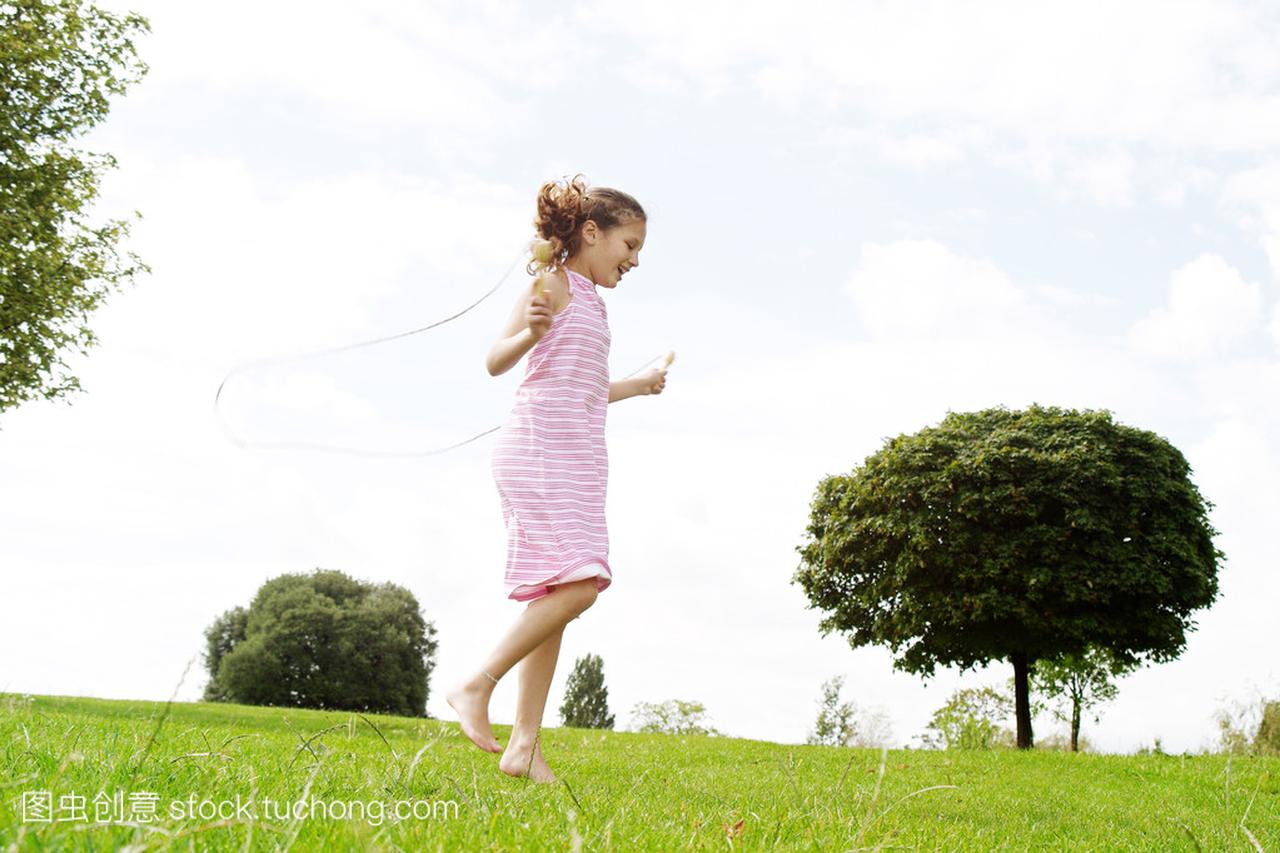 配置文件视图玩跳绳在公园里,一个年轻女孩的