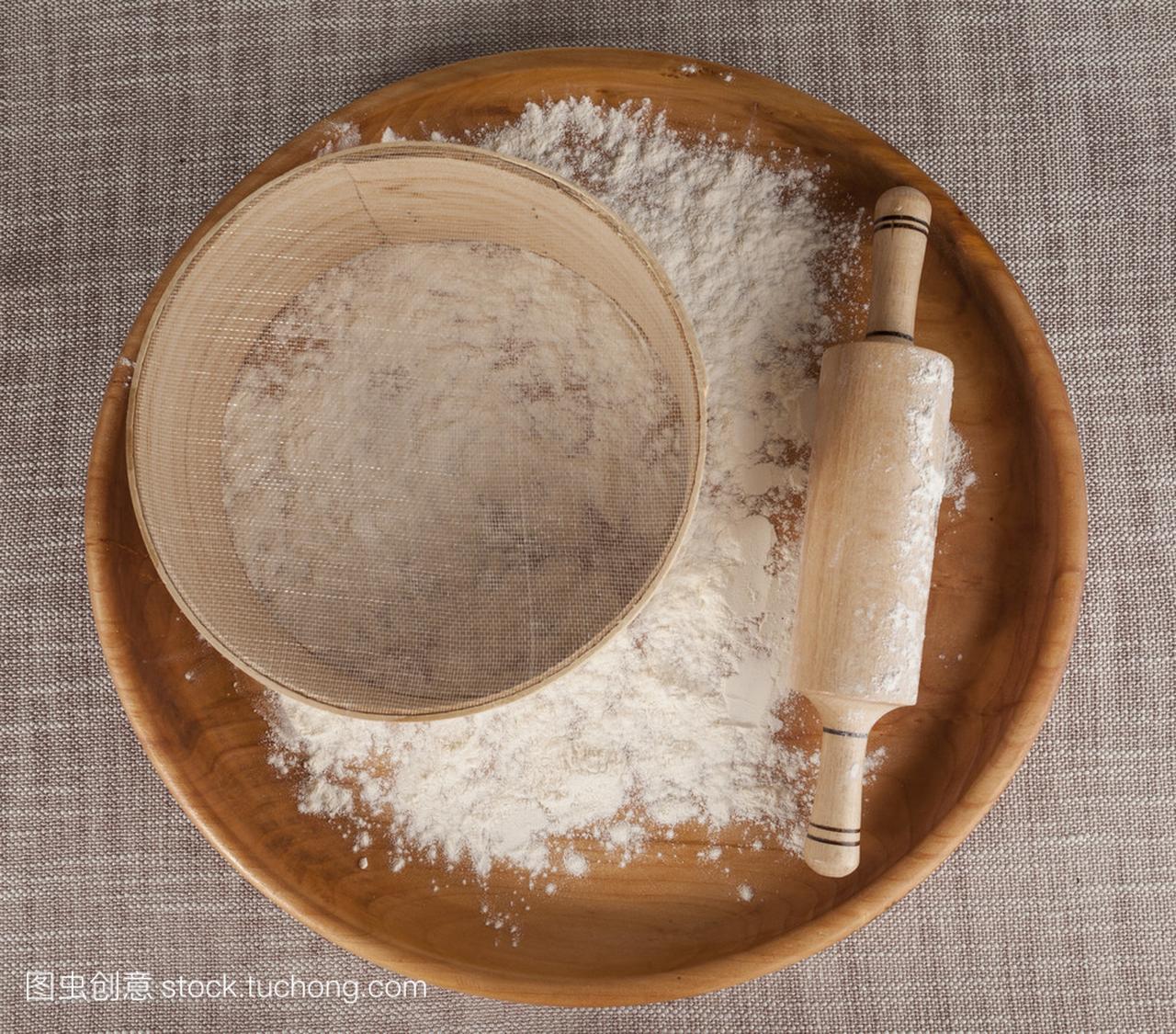 Rolling pin and sieve in the flour on a wooden tray.