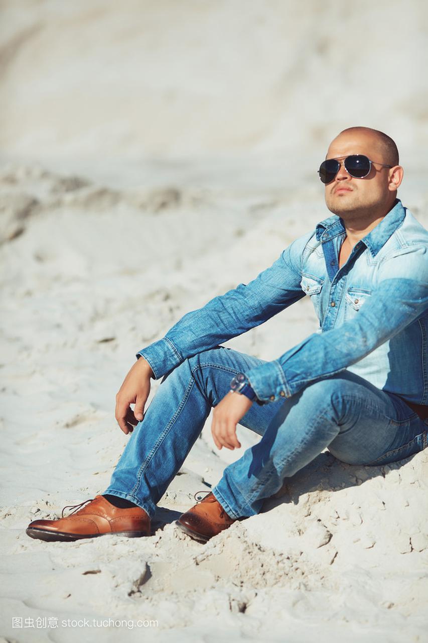 时尚的男人,穿着牛仔裤坐在沙上,戴着眼镜