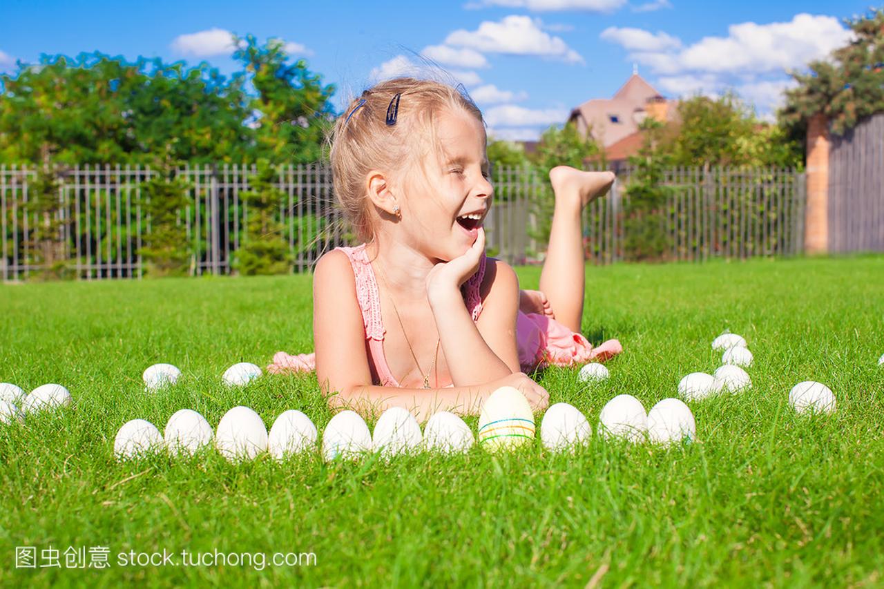 小小快乐的女孩玩白色的复活节蛋在绿色草地上