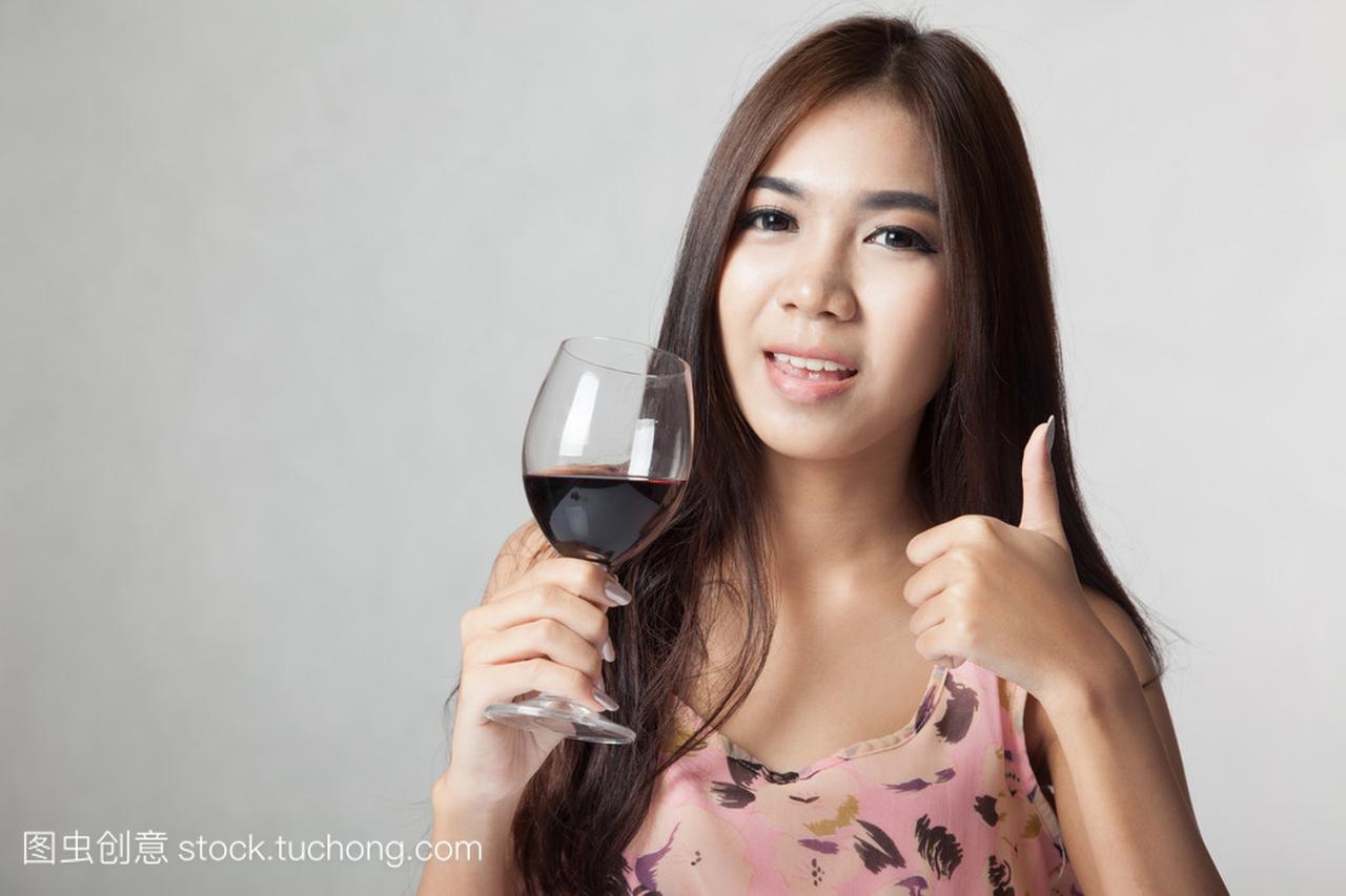 美丽的亚洲女人表明持有杯红酒竖起大拇指