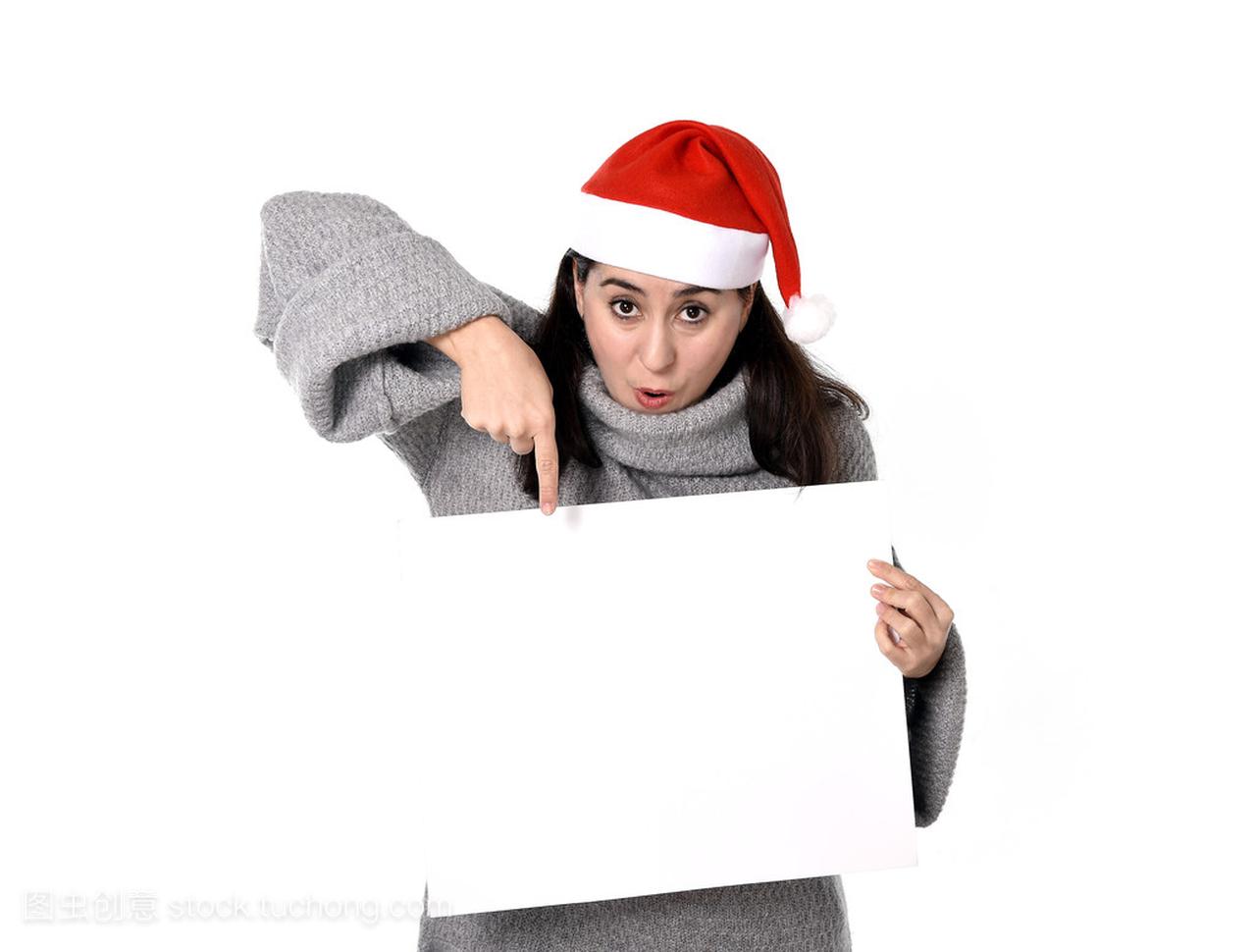 轻甜美拉丁女人在圣诞老人帽子指向空白广告牌