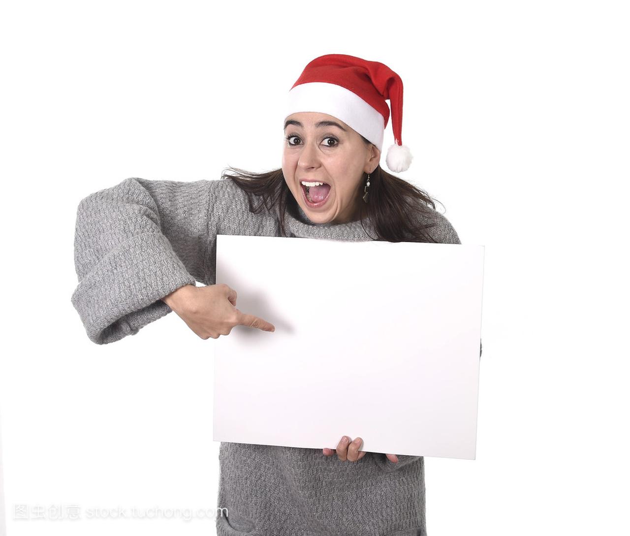 轻甜美拉丁女人在圣诞老人帽子指向空白广告牌