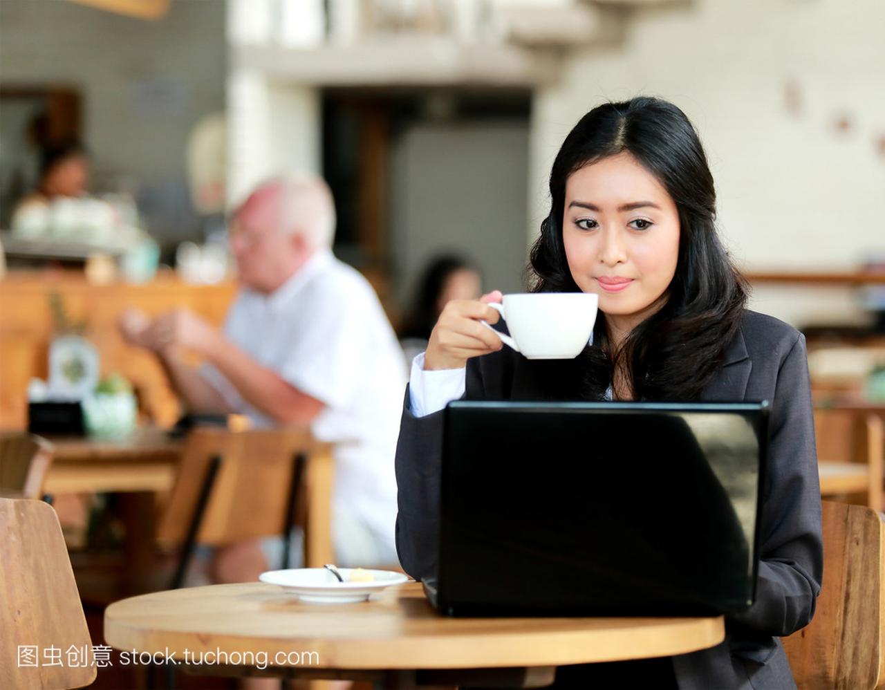 女商人在笔记本电脑上工作时喝咖啡