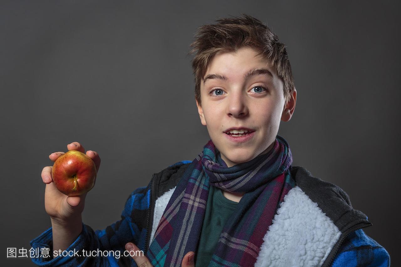 一位男性少年吃一个苹果与冬季夹克的肖像