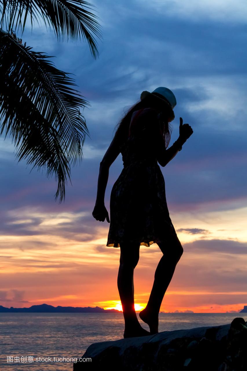 轮廓的热带日落背景在海边岩石上跳舞的女孩