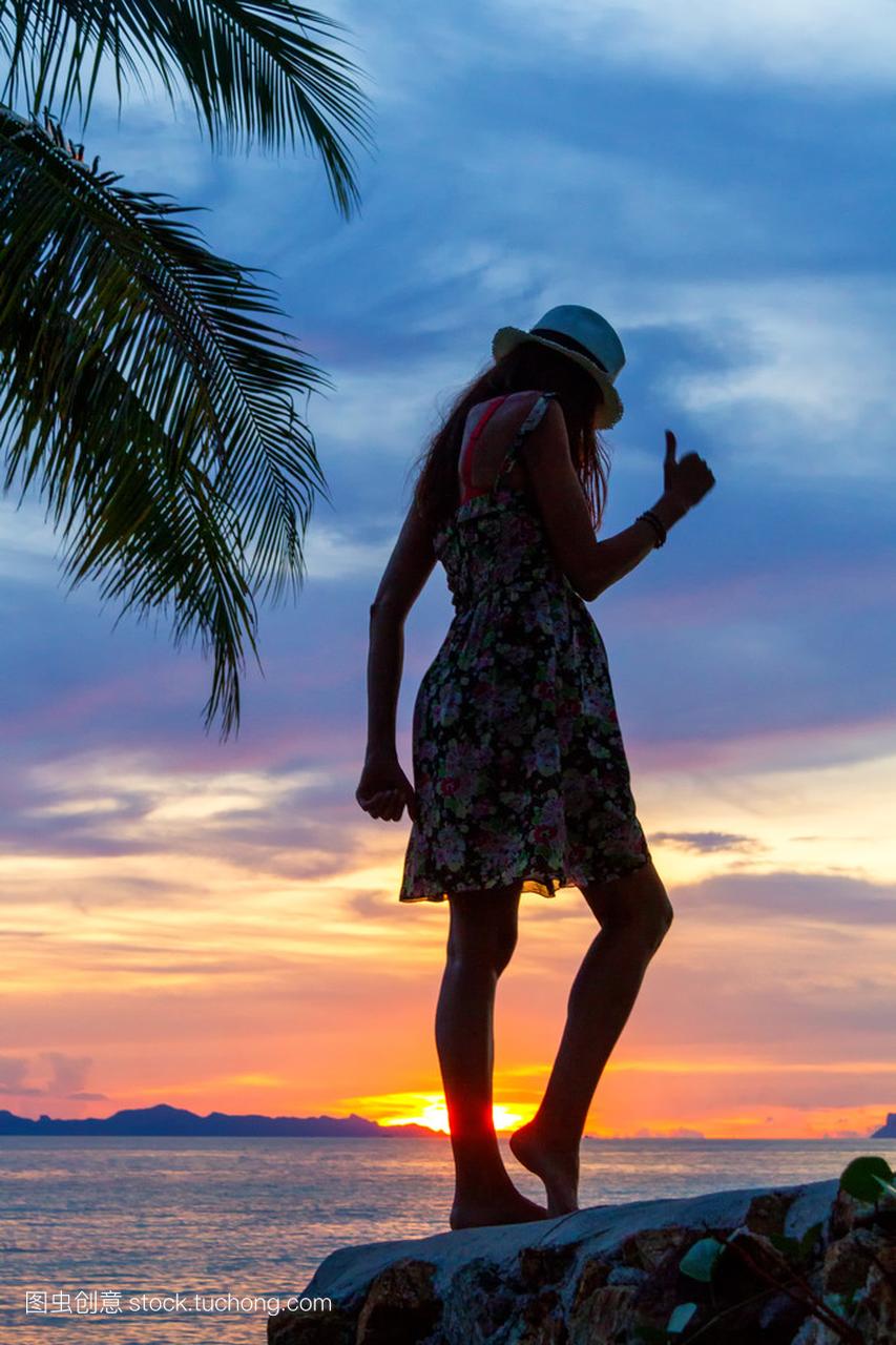轮廓的热带日落背景在海边岩石上跳舞的女孩