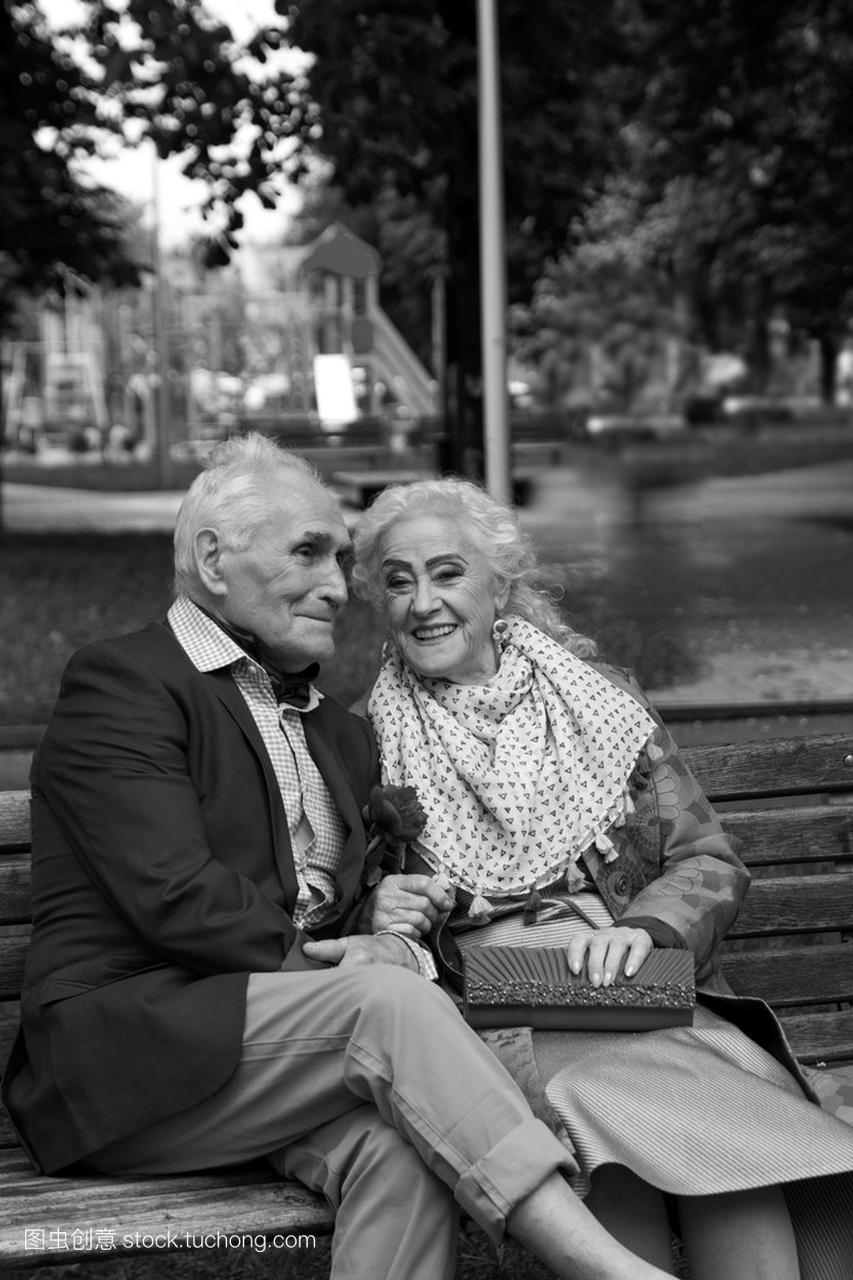 在公园的长椅上聊天的老年夫妇。黑色和白色