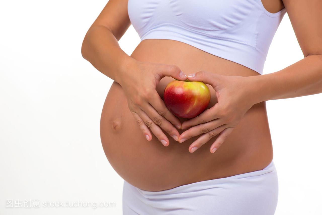 孕妇的肚子和苹果的特写镜头。手折的心。在白