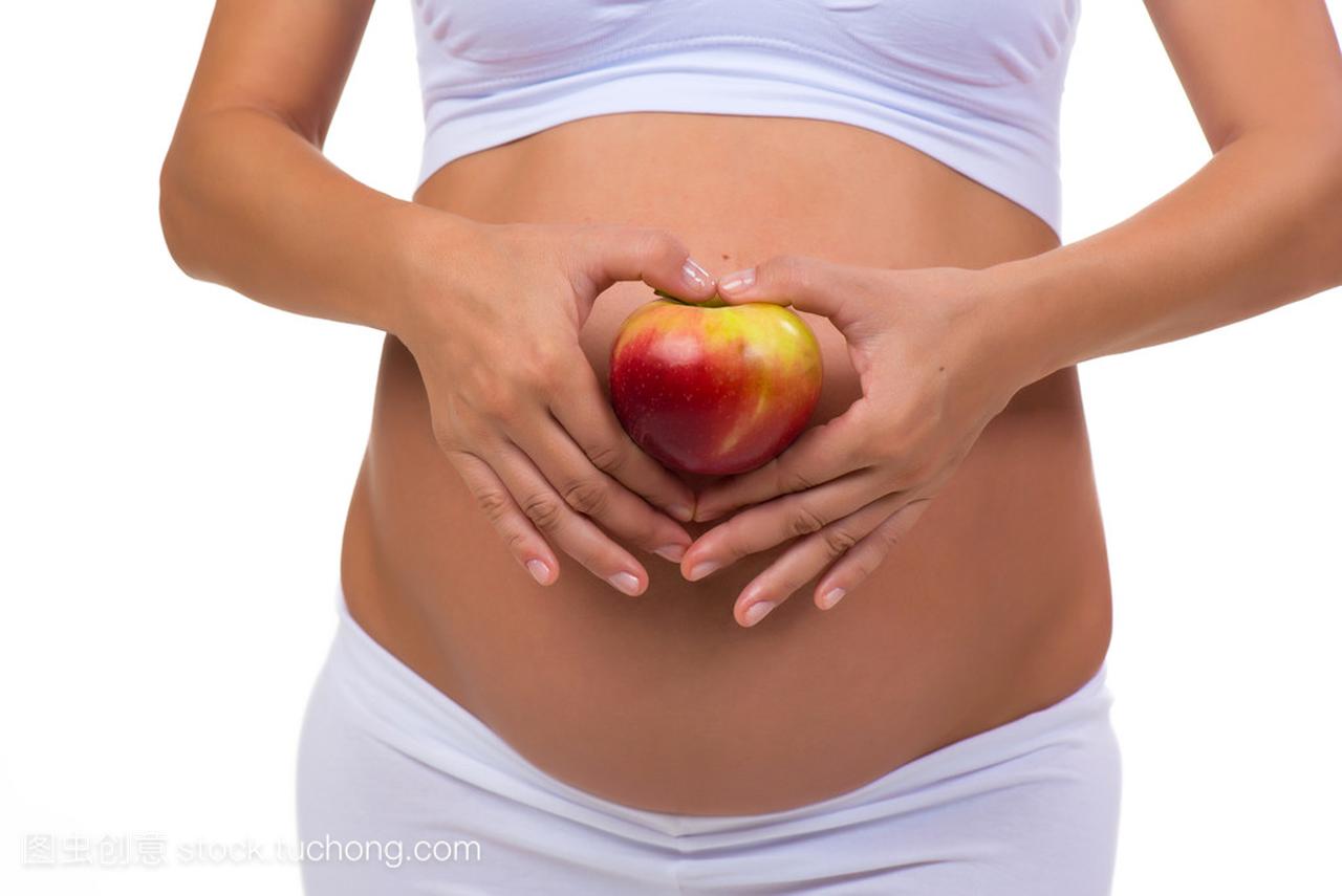 孕妇的肚子和苹果的特写镜头。手折的心。在白