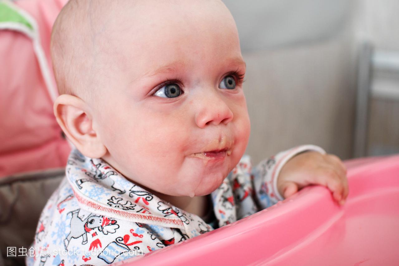 漂亮的宝宝吃粥从妈妈的手。他坐在粉红色的儿
