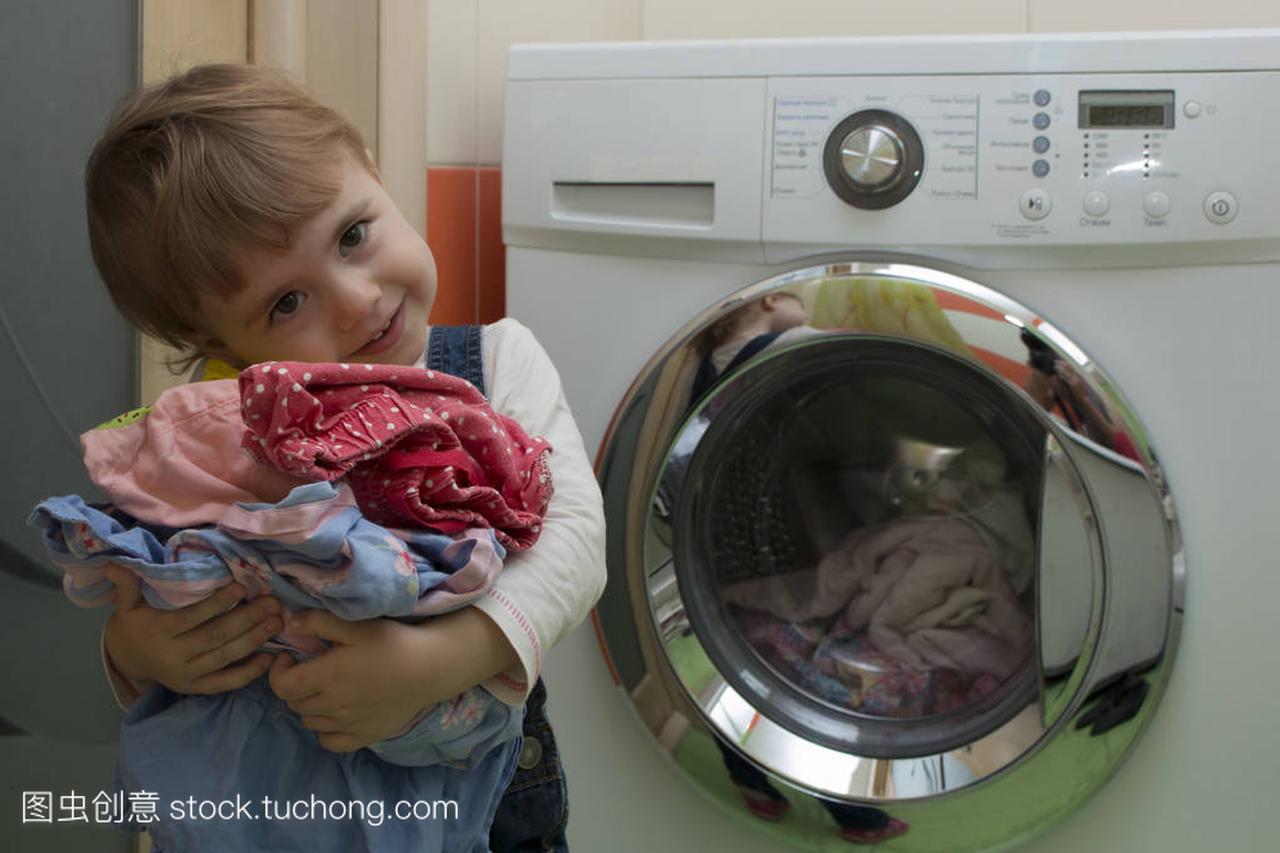 快乐可爱的小女孩洗衣服在家庭内部的衣服