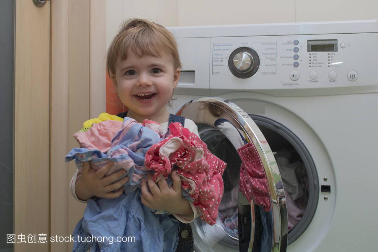 快乐可爱的小女孩洗衣服在家庭内部的衣服