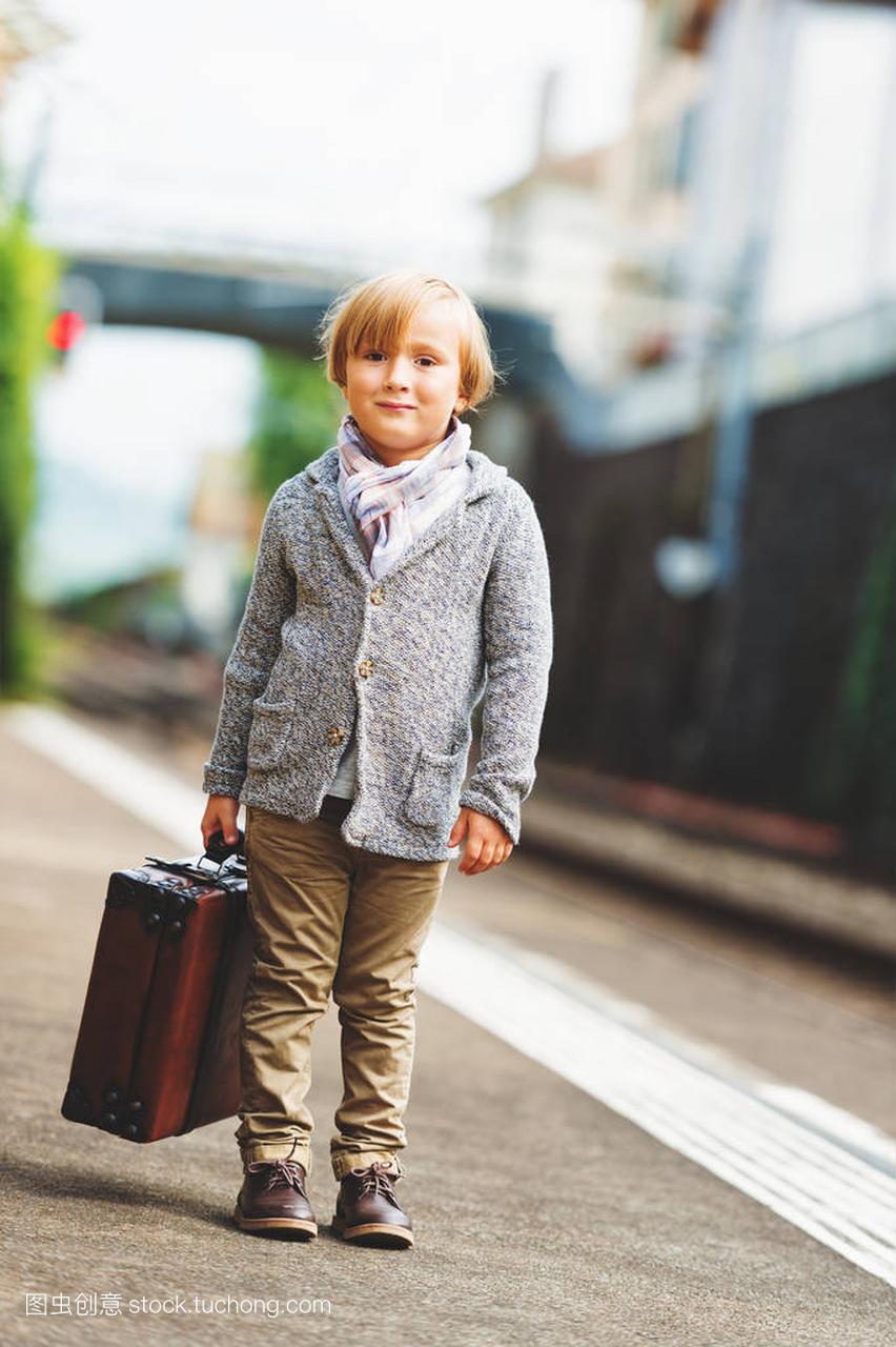 可爱的小男孩上一铁路站,等待火车带着手提箱