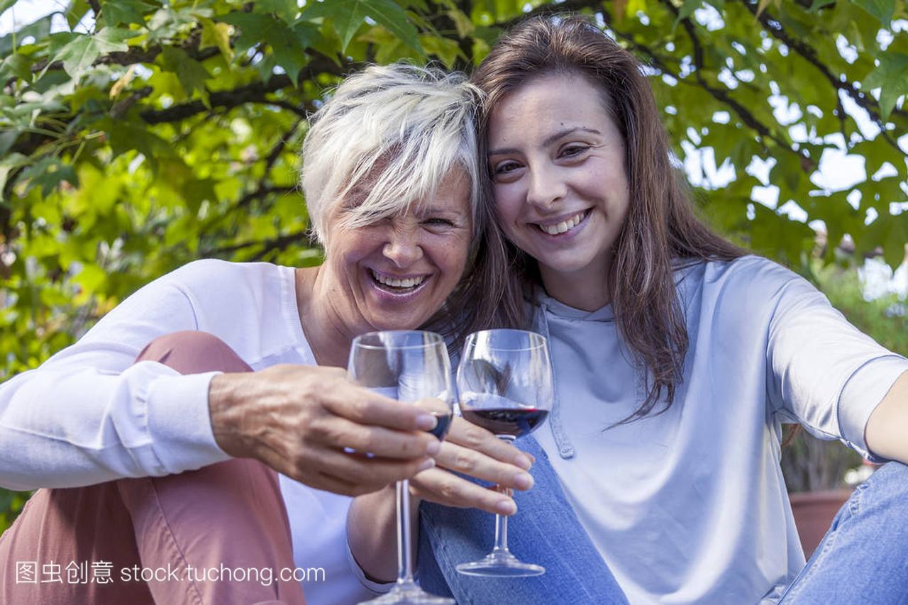 母亲和成年女儿品尝红酒坐在一棵大树