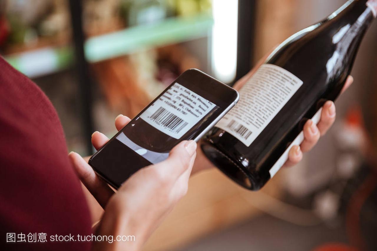 扫描条码与葡萄酒瓶上的移动电话的女人