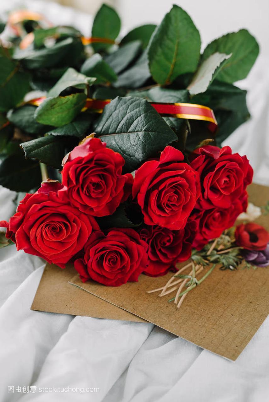 一束红玫瑰,祝贺在背景上的亚麻布信封