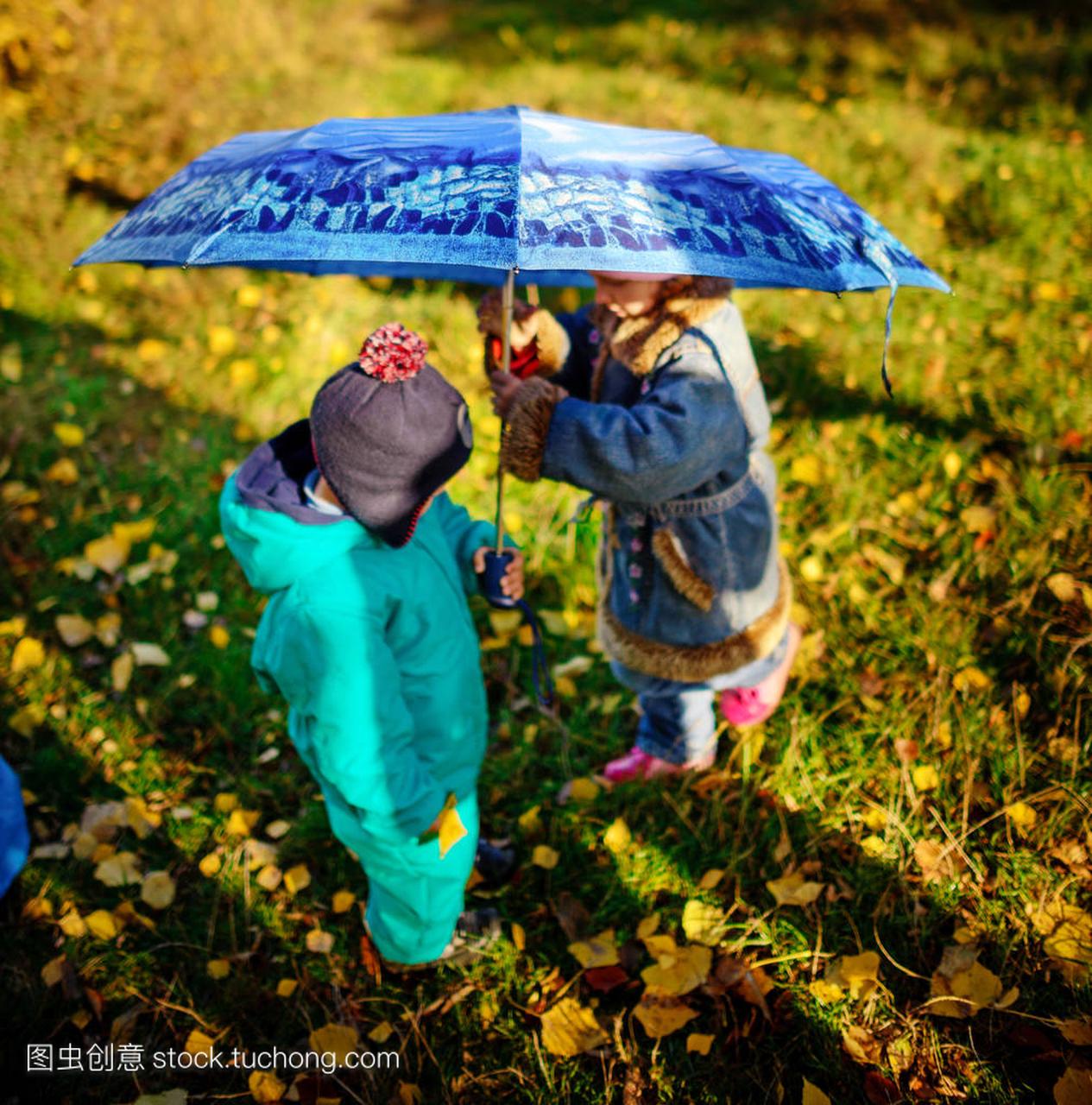 小女孩和男孩用伞在雨中玩。孩子们玩户外时间