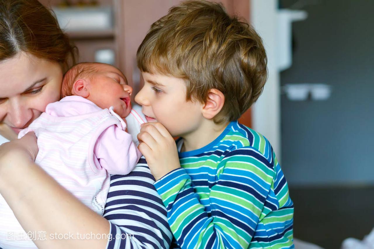 小家伙男孩接吻新生儿的妹妹。母亲抱着婴儿的