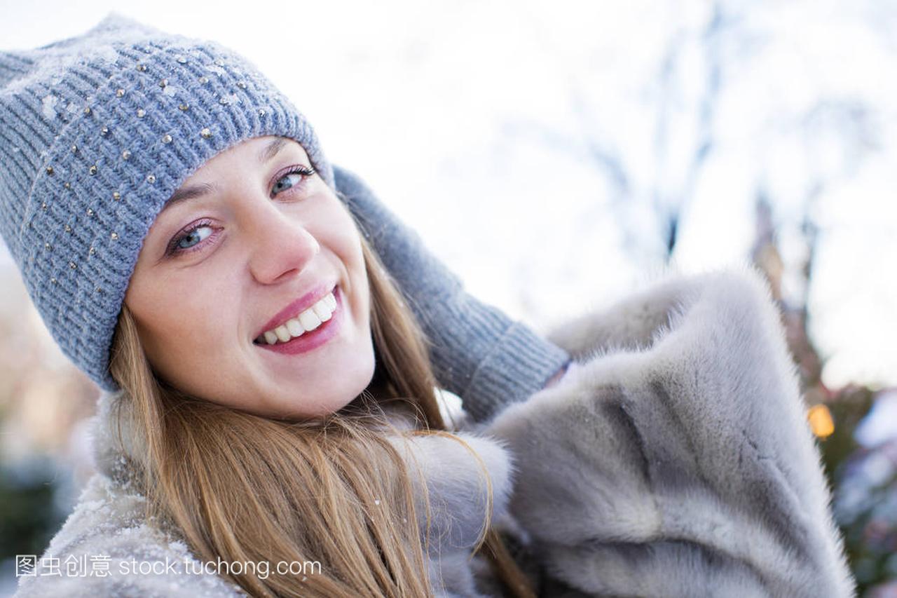 蓝色针织的帽子和灰色貂皮大衣的年轻女子
