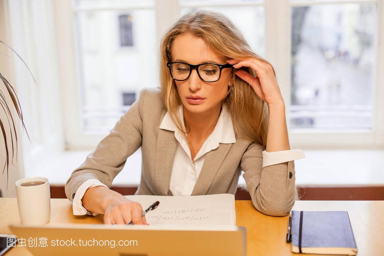 吸引年轻金发画卷戴眼镜和使用笔记本电脑。女