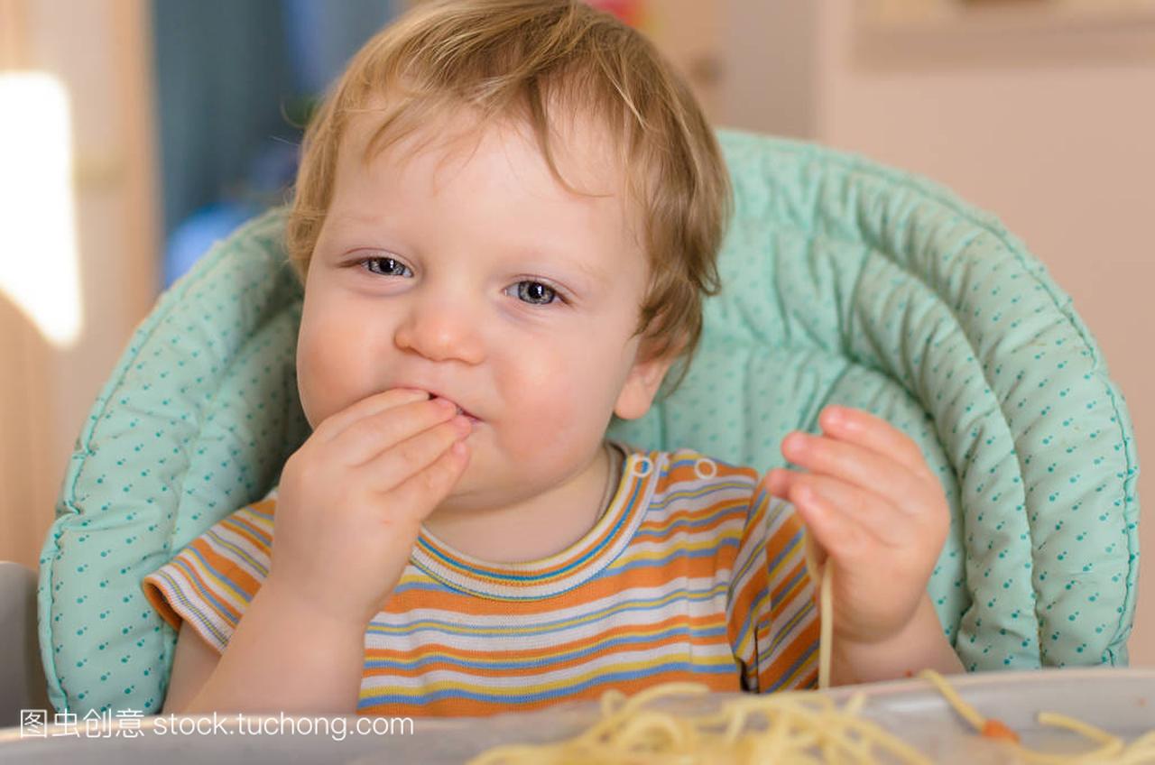 可爱的一岁宝宝吃意大利面条在儿童椅