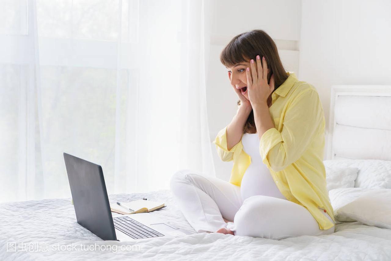 一名欧洲孕妇与黄色衬衫已从屏幕的笔记本电脑