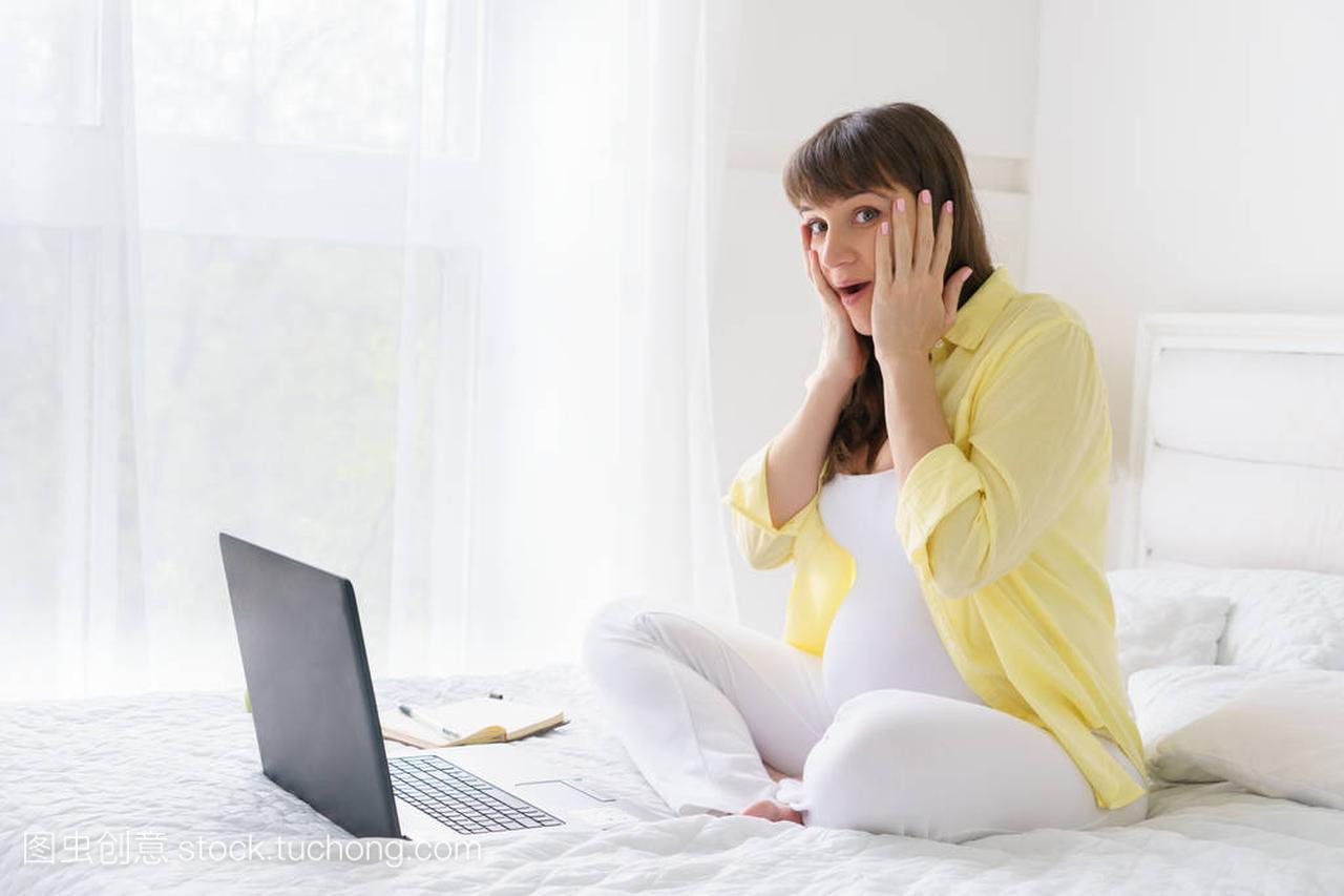一名欧洲孕妇与黄色衬衫已从屏幕的笔记本电脑