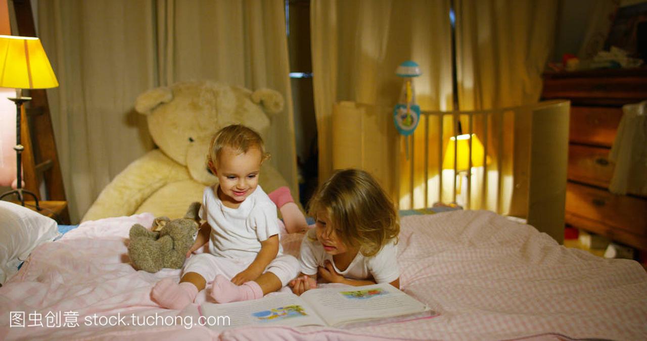 快乐和幸福的小女孩阅读在父母的床上玩。快乐