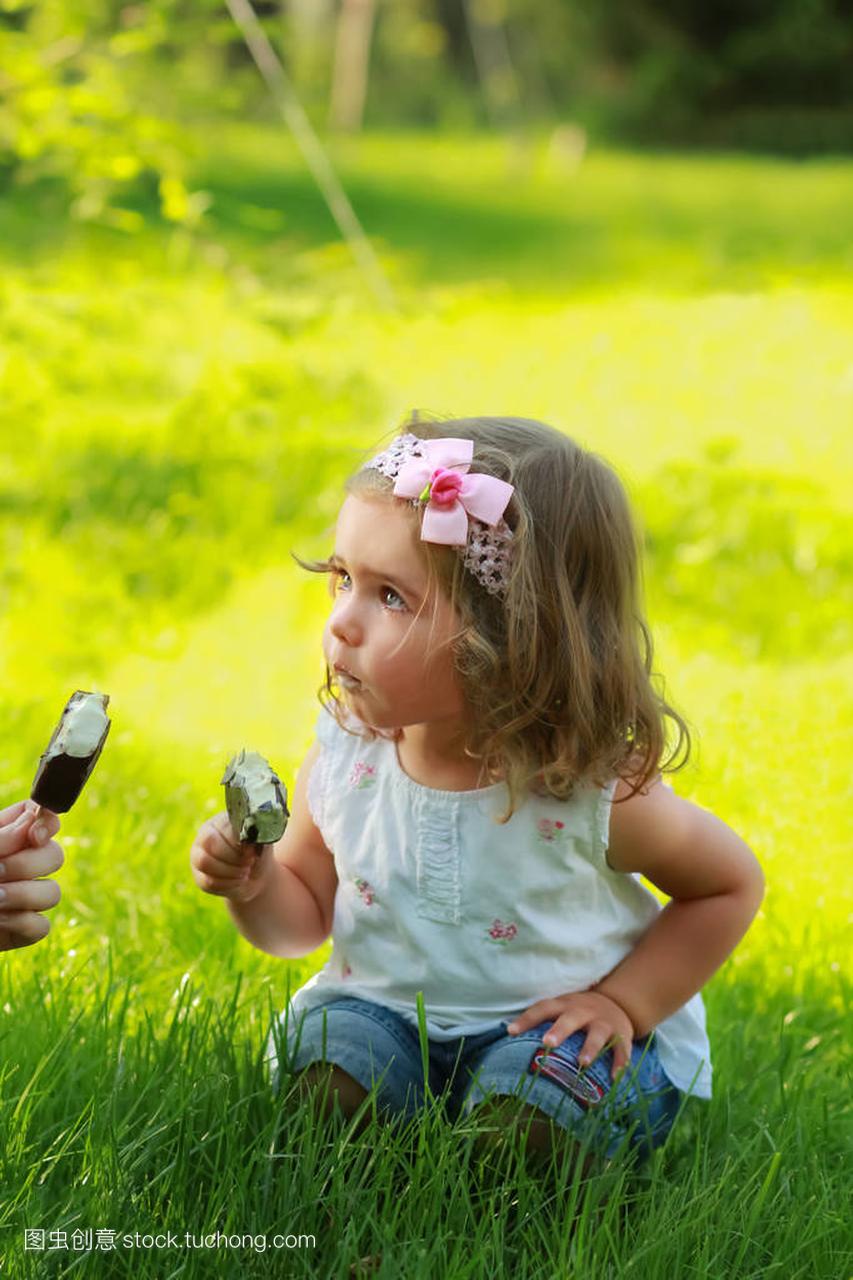 甜甜一岁女孩吃冰淇淋坐在公园的草坪上