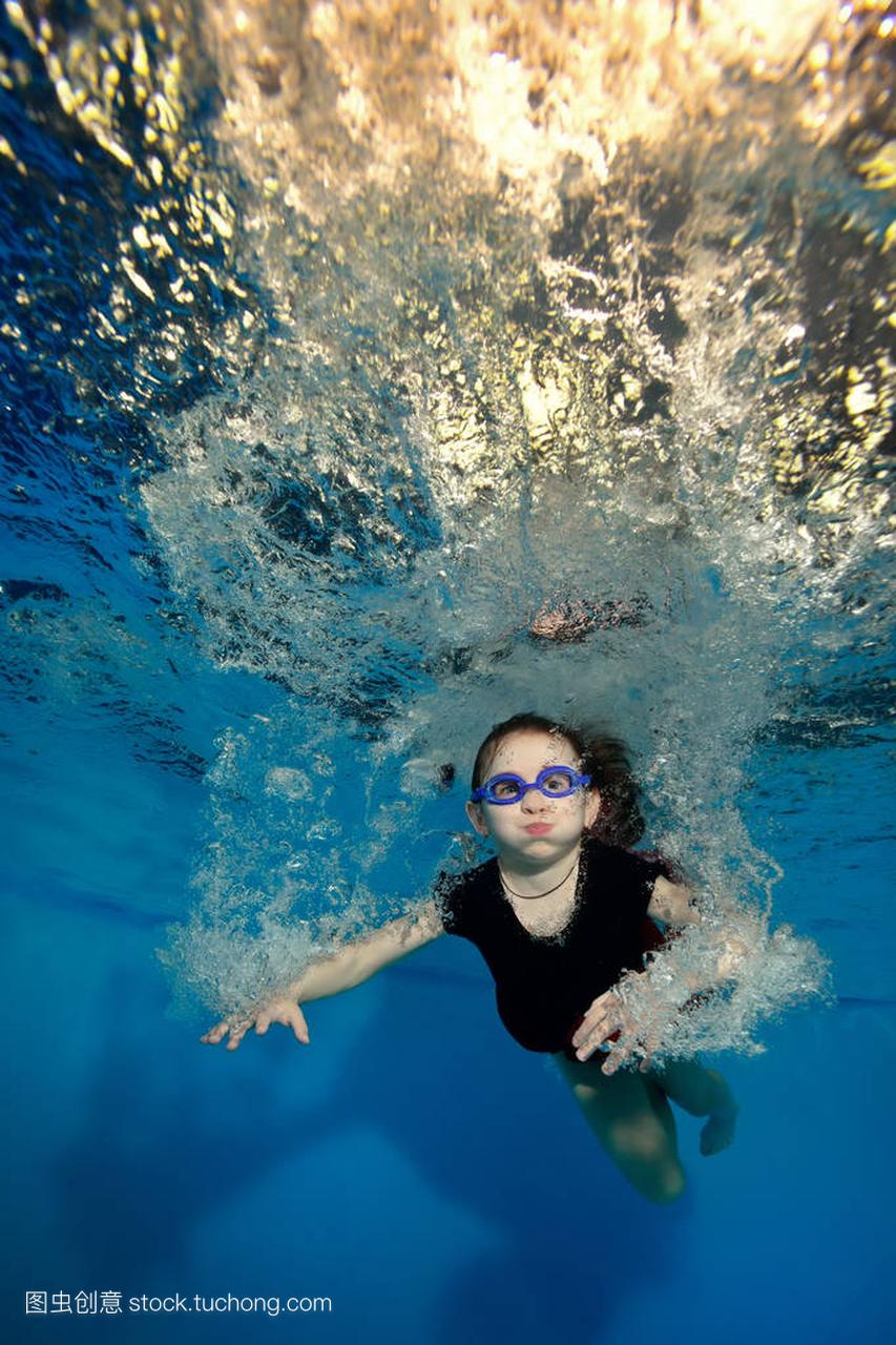 快乐的小女孩,游泳和打水下气泡在蓝色背景上