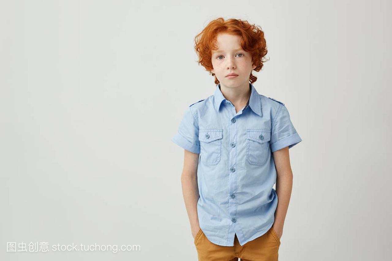 美丽的小男孩与生姜的头发和雀斑手在口袋里看