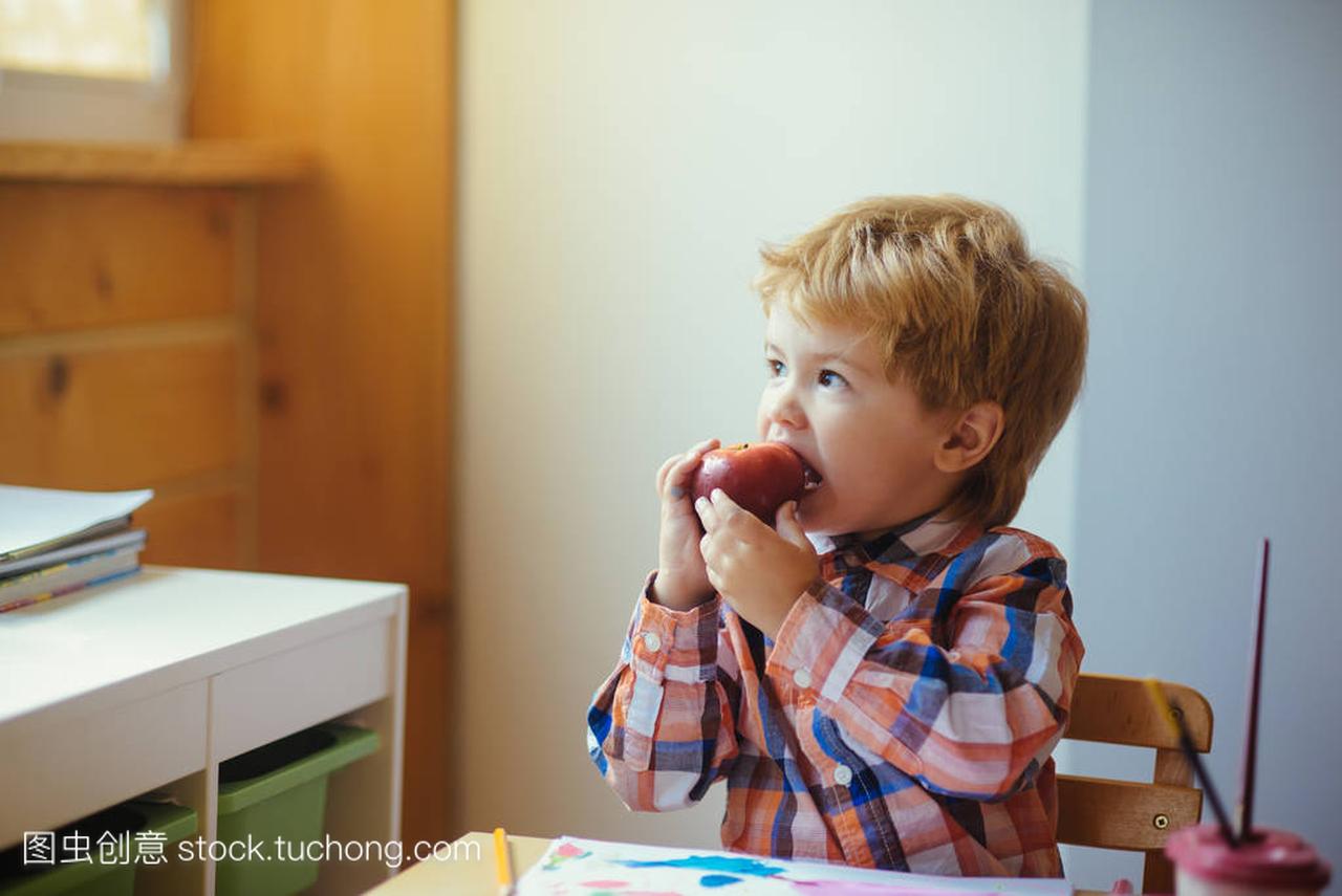 男孩吃苹果, 抬头看画。快乐健康的婴儿在幼儿
