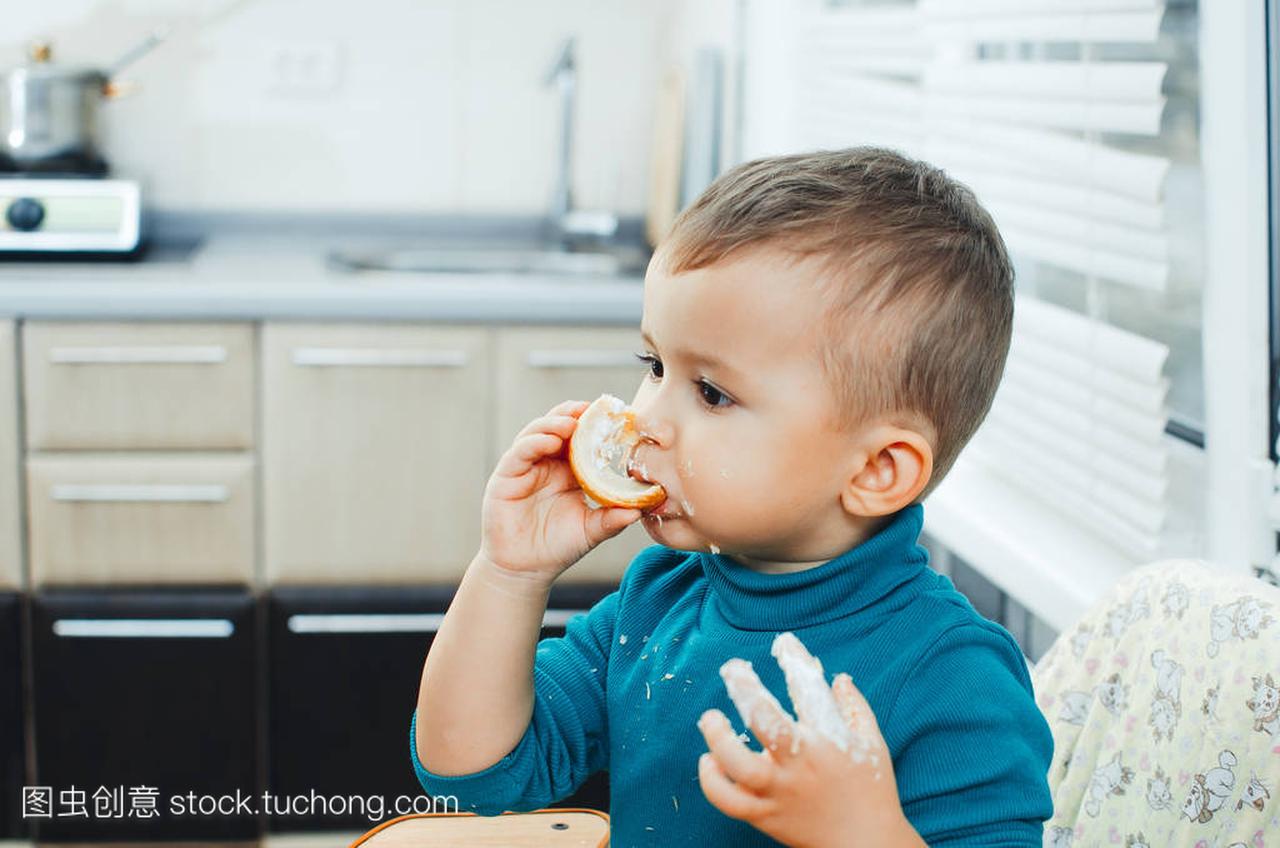 婴儿在厨房急切地吃美味的奶油角, 香草奶油