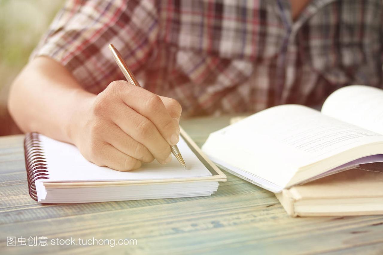 人的手、学生写字和笔记在木桌上与拷贝空间,