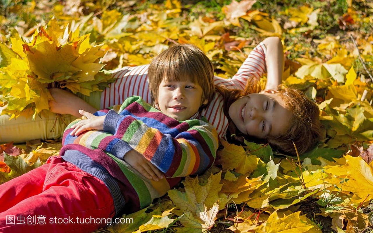 一个男孩和一个女孩躺在公园的黄叶子上