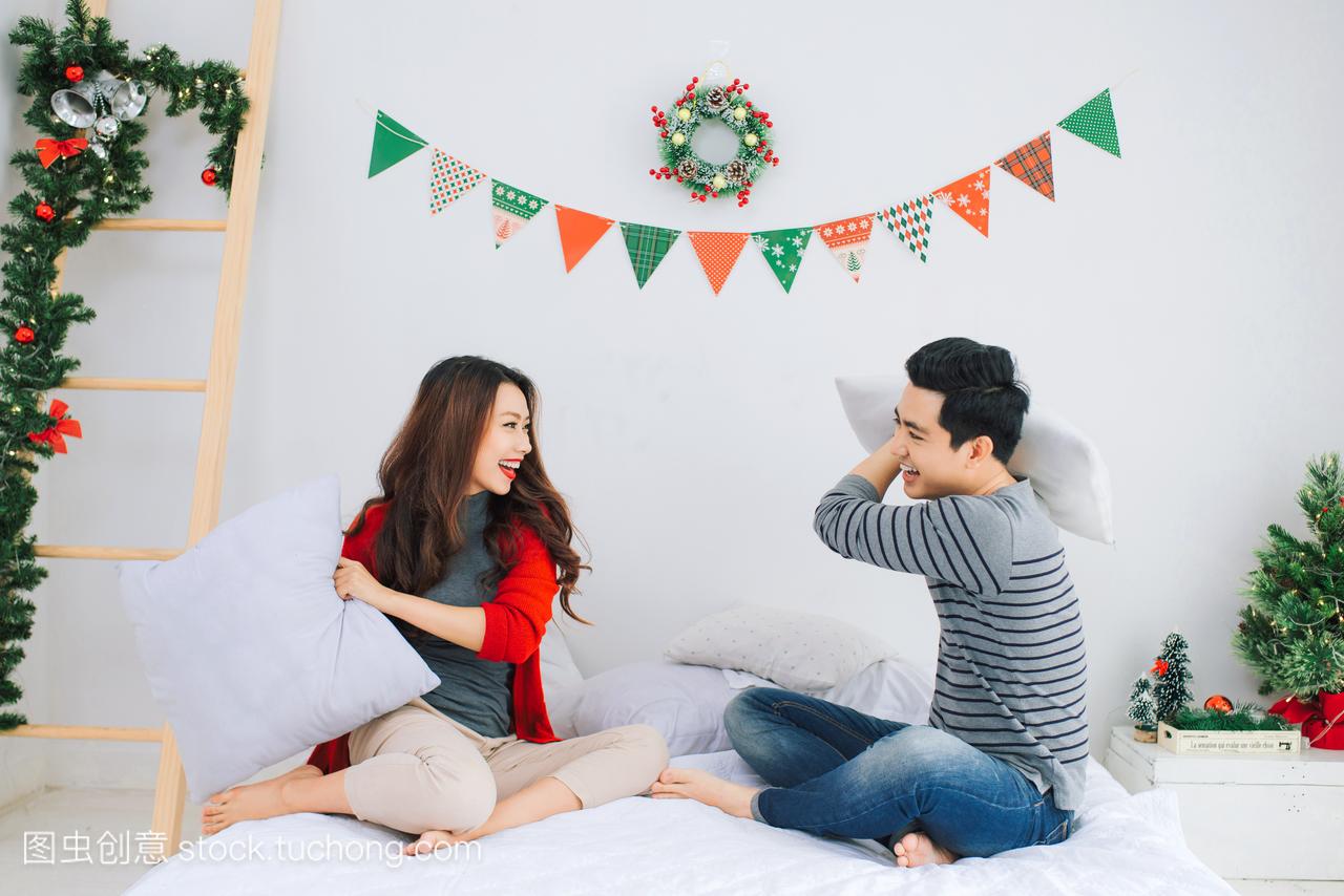 亚洲夫妇坐在床上打架枕头在圣诞节装饰的房间