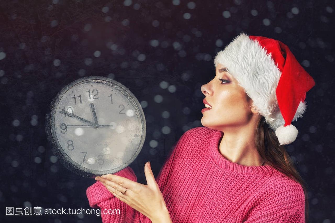 年轻妇女拿着时钟表示圣诞节的时间
