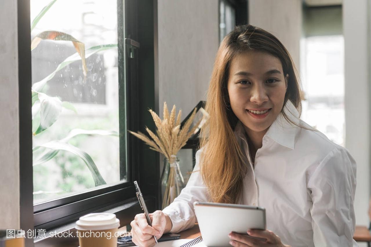 年轻的女商人穿着白裙子坐在咖啡馆的餐桌旁,