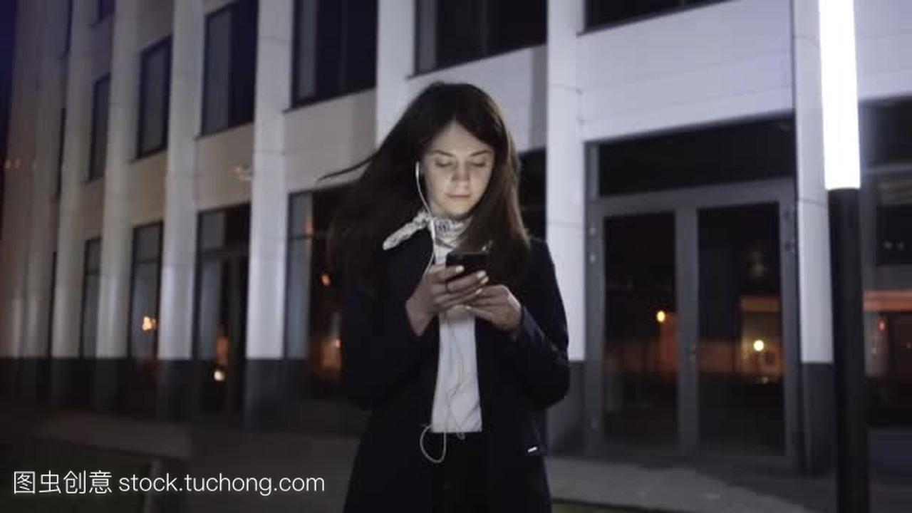 一个年轻的女实业家在一个晚上城市的智能手机