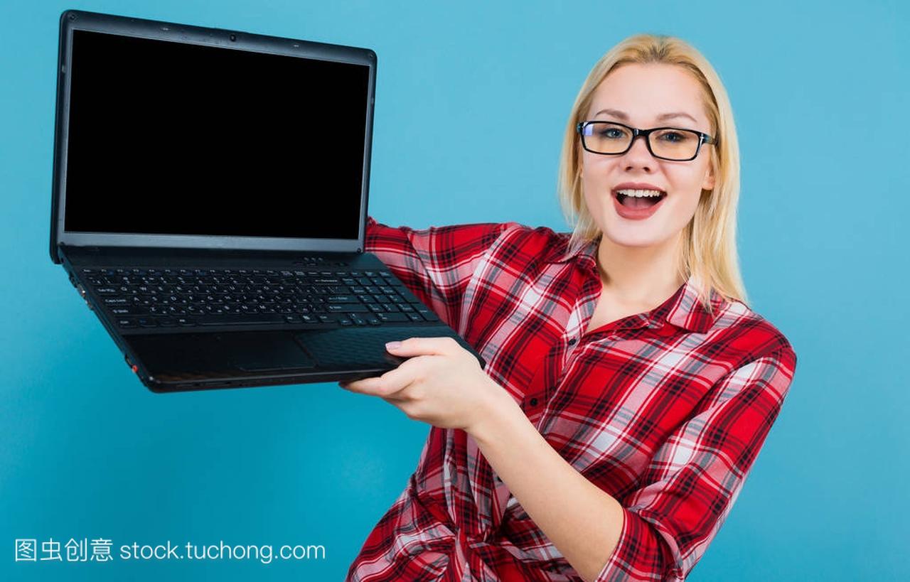 在蓝色背景下手持现代笔记本电脑的美丽年轻女