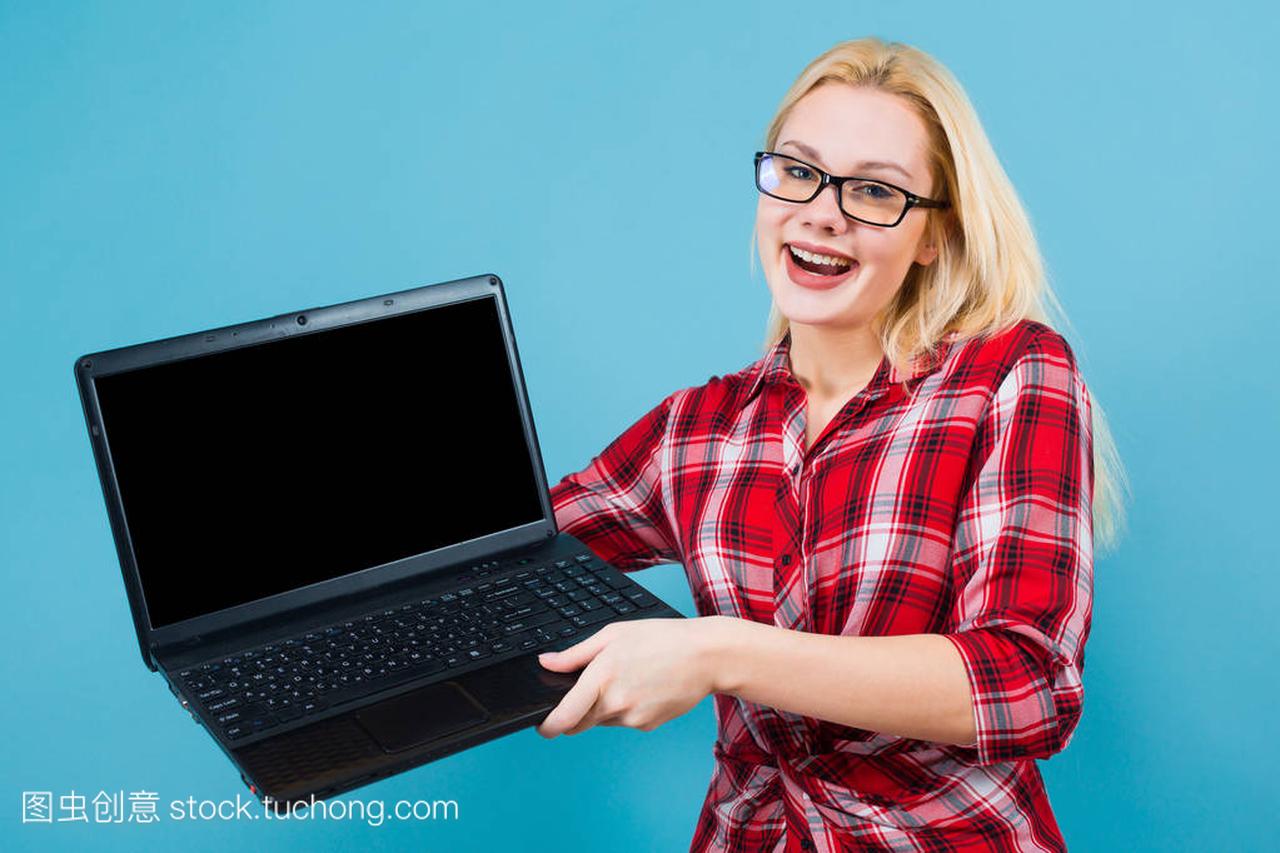在蓝色背景下手持现代笔记本电脑的美丽年轻女