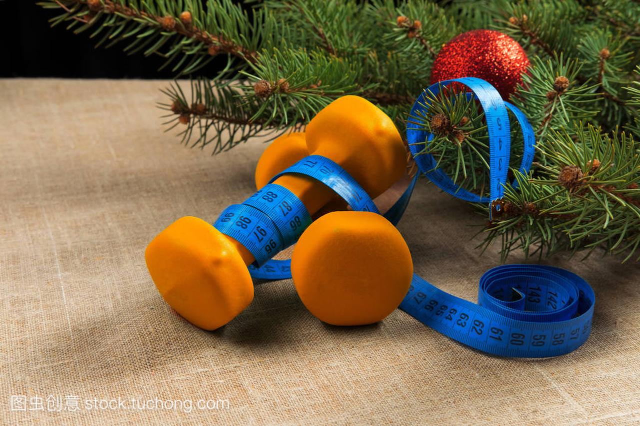 两个橙色哑铃健身圣诞树用红色新年球和测量磁