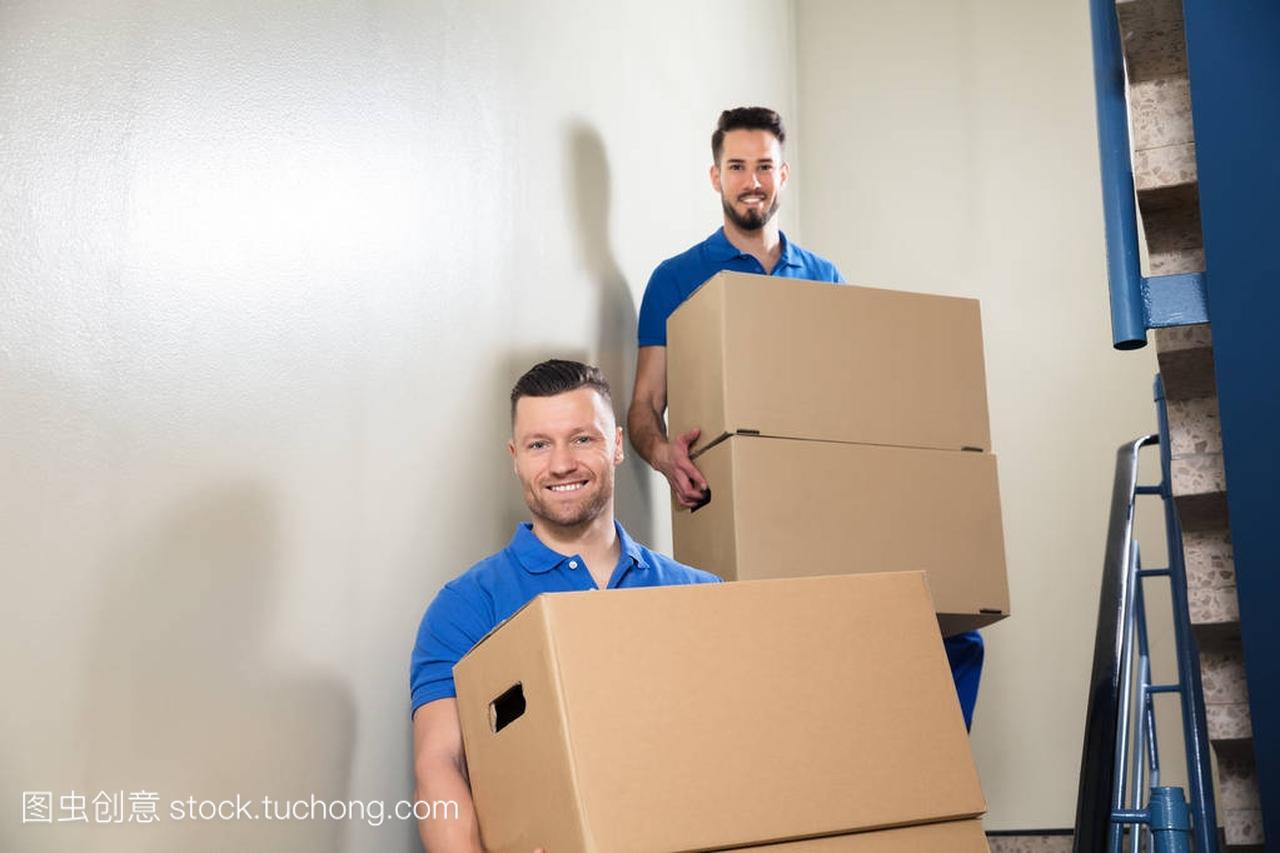 两名年轻男性搬运工在楼梯上背着纸板箱的蓝色