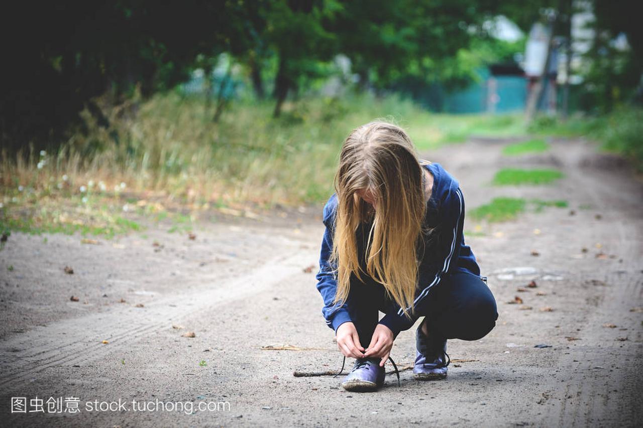 乡村道路上的体育女孩把鞋带系在运动鞋上