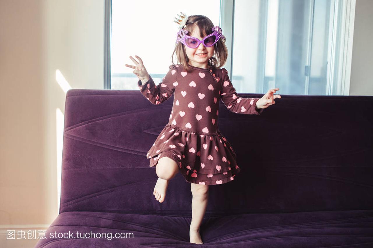 滑稽可爱的小女孩的肖像在沙发上跳跳舞在室内